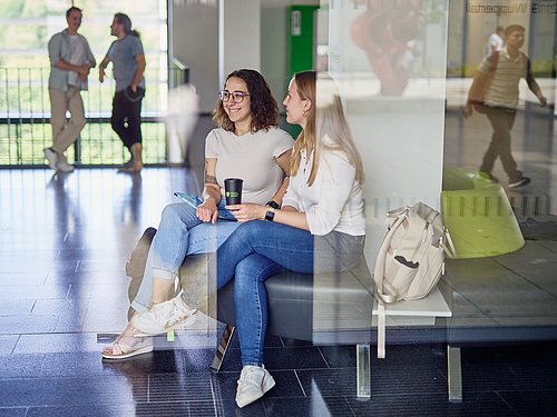 Zwei Studentinnen im Foyer sitzend, durch Glasscheibe fotografiert