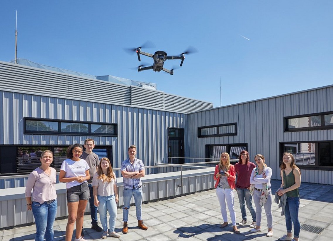 Studierende testen unter freiem Himmel mit ihrer Dozentin eine Drohne