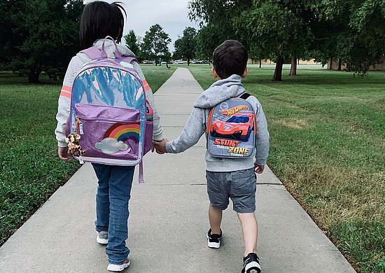 Zwei Kinder mit Ranzen auf dem Rücken gehen zu Schule 