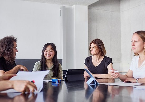 Diverse Studierende und Lehrende diskutieren gemeinsam an einem Tisch 