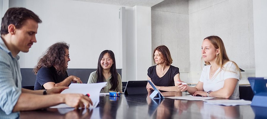 Diverse Studierende und Lehrende diskutieren gemeinsam an einem Tisch 