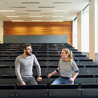 zwei junge Dozierende in einem leeren Hörsaal im Gespräch